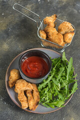 Chicken nuggets on a plate with herbs and tomato sauce and in a deep-frying basket vertical arrangement