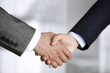 Business people in office suits standing and shaking hands, close-up. Business communication concept. Handshake and marketing