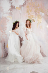 Two charming brides in beautiful spring wreaths on their heads. Beautiful young women in wedding dresses