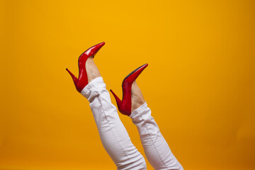 Female feet in beautiful red stiletto shoes, yellow background copy space.