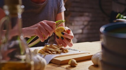 Woman peeling ginger and vegetables for cooking on kitchen table. Closeup hands. Cosy dark room. Real, authentic cooking. 