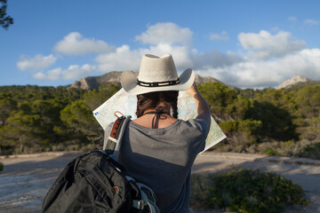 A woman hiking in the mountains of Majorca. A hiker looking at the map while traveling on the island of majorca. The girl is wearing a hat and an Australian look, has long hair and two braids.