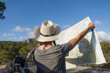 A woman hiking in the mountains of Majorca. A hiker looking at the map while traveling on the island of majorca. The girl is wearing a hat and an Australian look, has long hair and two braids.