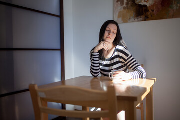 A calm young woman in a striped jacket is sitting at a table with a Cup of hot drink.
