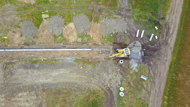 Bagger verlegt eine Leitung aus Rohren in einem Baugebiet, Baustelle aus der Vogelperspektive