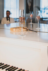 A glass transparent glass with rose wine stands on a white piano. Black and white keys are visible. behind a glass is a clutch bag and a cigarette with a mouthpiece. A glass stands in a beautiful room