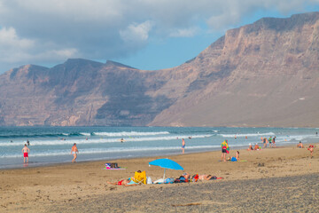 Fototapeta na wymiar Famara Beach, popular surfing beach on coast in Lanzarote. Canary Islands. Spain. Sand dunes and people on the beach