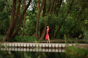 Fototapeta premium A girl walks in a beautiful city park in the summer. walk after the rain. red dress, red shoes