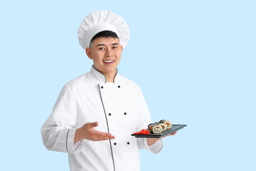 Handsome Asian chef with sushi rolls on color background