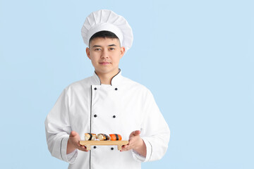 Handsome Asian chef with sushi rolls on color background