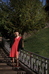 girl in a red dress and a men's black jacket in the park in the summer. The sun is shining. the model descends the steps. stylish urban clothing