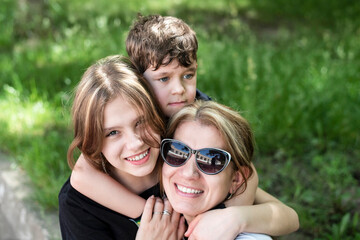 Fototapeta premium A woman in sunglasses hugs her children and they smile and relax together while walking and playing outdoors