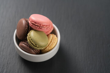 assorted macarons in white bowl on slate background with copy space