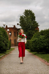 girl in red pants walks around the city with a bouquet of peonies