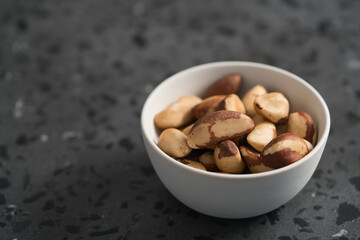 Brazil nuts in white bowl on concrete background with copy space