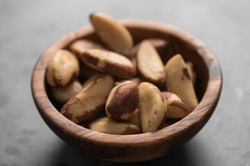 Brazil nuts in olive wood bowl on concrete background closeup