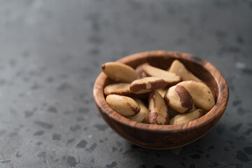 Brazil nuts in olive wood bowl on concrete background with copy space