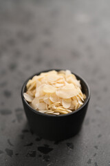 Almond flakes in small black bowl on concrete background