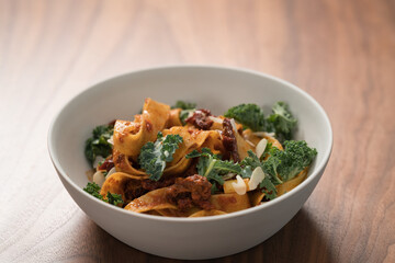 fettuccine pasta with sun-dried tomatoes, almond flakes and kale leaves in white bowl on walnut table