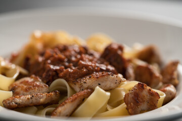 fettuccine pasta with fried chicken and sun-dried tomatoes in white bowl closeup