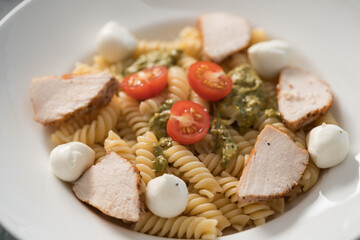 fussili pasta with chicken fillet, tomatoes, mozzarella and pesto sauce in white bowl closeup