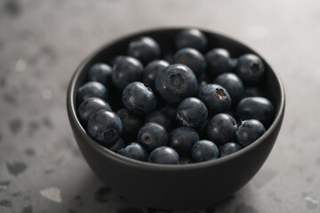 Ripe blueberries in black bowl on concrete background closeup