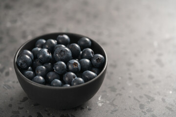 Ripe blueberries in black bowl on concrete background with copy space