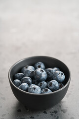 Ripe blueberries in black bowl on concrete background with copy space