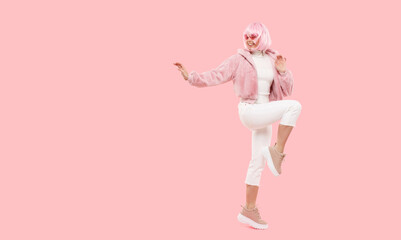 Full length photo of young happy teenage girl dancing at party, jumping and moving arms, looking to copy space on left, isolated on pink background