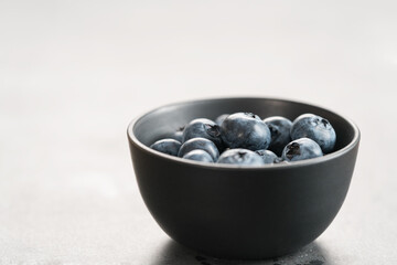 Ripe blueberries in black bowl on concrete background with copy space
