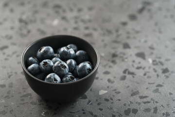 Ripe blueberries in black bowl on concrete background with copy space