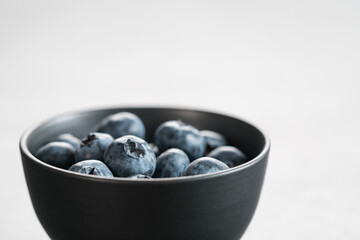 Ripe blueberries in black bowl on concrete background with copy space