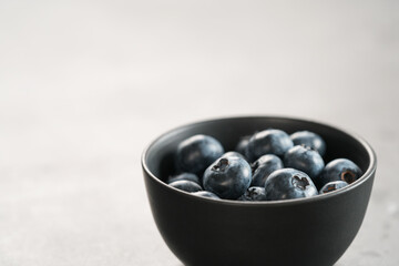Ripe blueberries in black bowl on concrete background with copy space