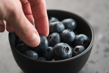 Man hand pick ripe blueberries from black bowl on concrete background closeup