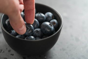 Man hand pick ripe blueberries from black bowl on concrete background closeup