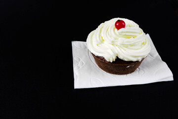 side-view gluten-free cupcake with cream cheese and red currant on a white napkin on a black background . homemade baking