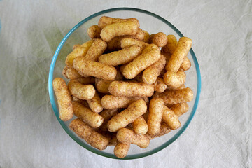 glass bowl with gluten-free corn sticks with cocoa on a beige tablecloth top view . sweet Breakfast snacks for children