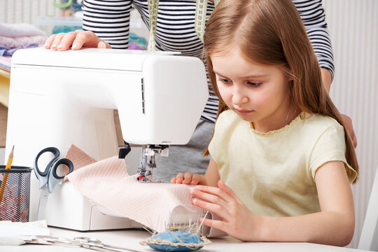 little girl carefully working with modern sewing machine