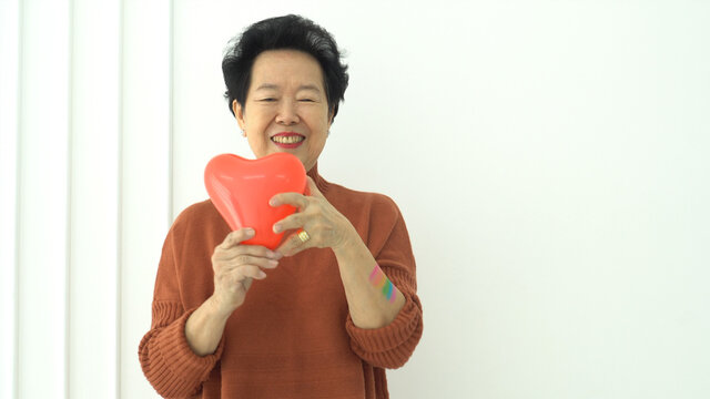 Asian elder mother support LGTBQ children smile with rainbow pride paint and balloon heart