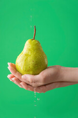 Female hands washing pear on the green saturated background. Concept of the importance of washing vegetables