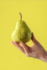 Female hands washing pear on the yellow saturated background. Concept of the importance of washing fruits