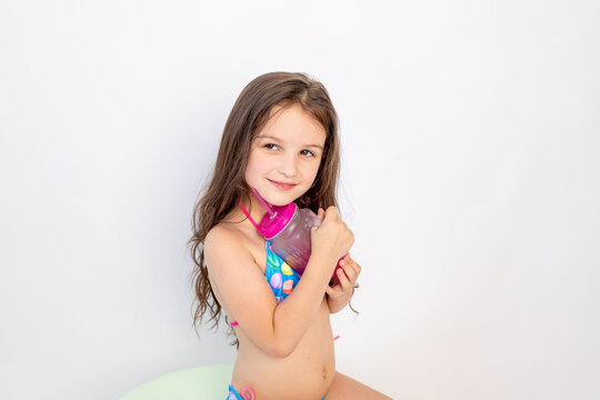 a little girl of 5-6 years old is sitting in a swimsuit with a cocktail on a white isolated background, a place for text