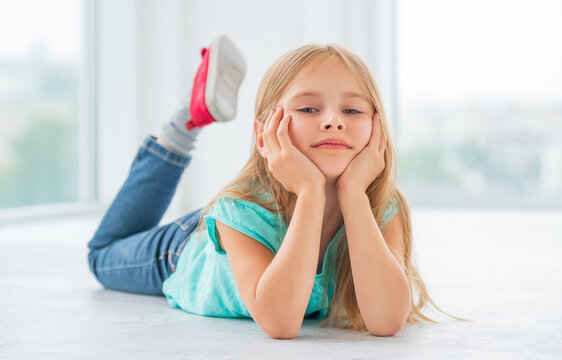 A blonde little girl in blue dress and fancy jeans lying on the floor on her stomach, relaxing