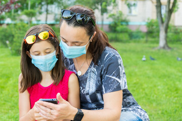 Mom with daughter in the park in medical masks. Family of mom and kid wearing protective medical...