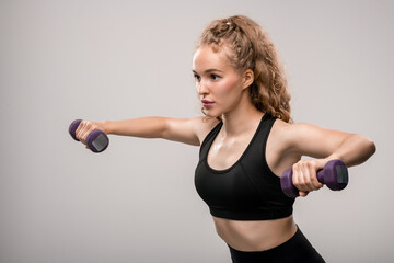 Pretty blond sportswoman in activewear exercising against grey background