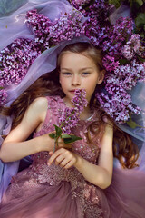 Fototapeta premium child girl in a purple floral dress lies on the ground among lilacs