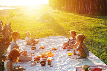 Kids having picnic on a lawn, lighted with a beautiful setting sun.