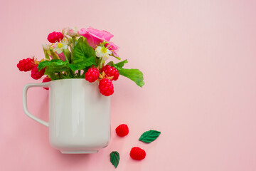 Flowers and berries in a white mug. I wish you a good day. Congratulations. Summer bouquet in a mug on a pink background. Space for text. Roses and raspberries in a mug.