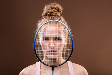 Serious sportswoman with blond hair looking at you from behind tennis racket