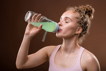 Young thirsty active woman with blond curly hair having refreshing drink